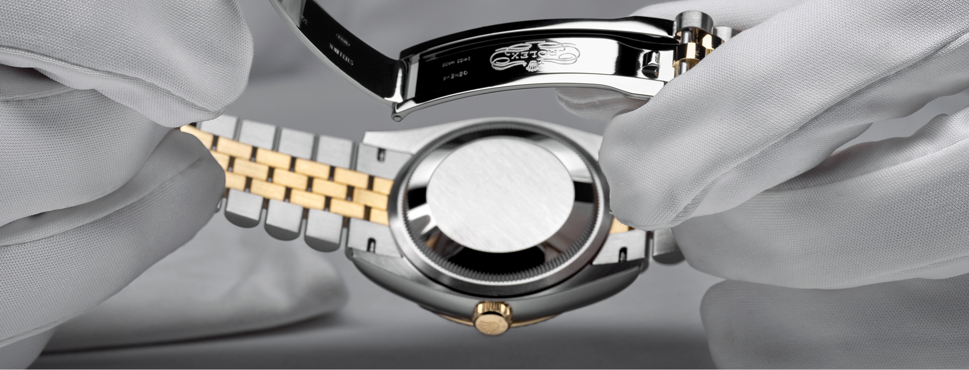 Gloved hands opening a Rolex Oyster bracelet clasp to reveal the case back