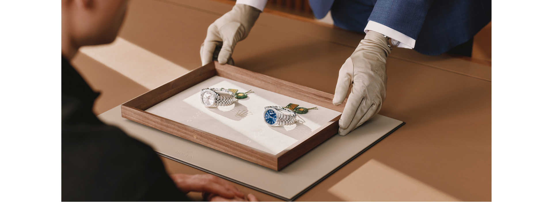 A specialist wearing gloves presenting Rolex watches on a wooden tray