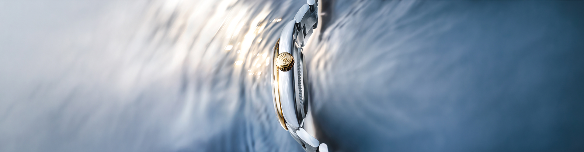 Side profile of a Rolex watch on water, with a gold crown catching the light