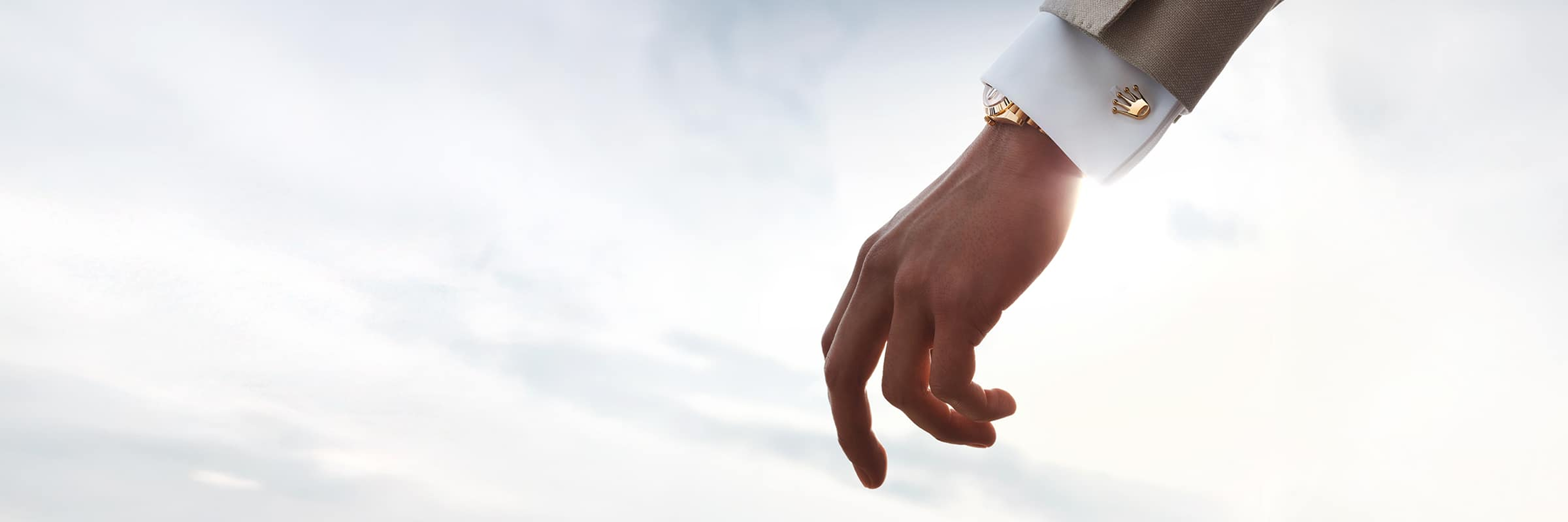 A person wearing Rolex Crown cufflinks, reaching towards the sky